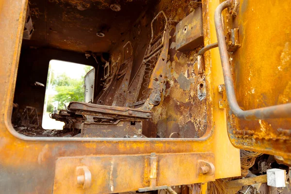 View inside the cabin of a burned-out military vehicle. Burnt chairs in the car. rusty military equipment