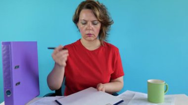 Kırk yaşında kırmızı tişörtlü bir kadın masada otururken kağıtlara bir şeyler yazıyor. Mavi arka planda yetişkin bir kadının portresi