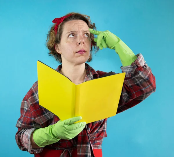 Thoughtful pin-up woman in a plaid shirt holds a yellow book in her hands on a blue background. Portrait of an adult woman. woman thinks