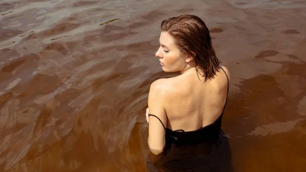 Rear view of a wet woman in a black dress in the water. Woman swimming in black dress