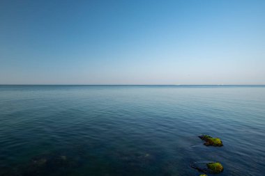 Karanlık deniz ve mavi gökyüzü manzarası. Düz ufuk. Denizde taşlar