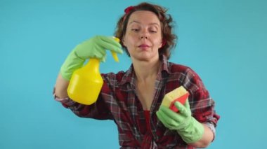 Adult cheerful pin-up cleaning woman in a plaid shirt in green gloves wipes with a washing sponge holds a yellow spray gun in her hands. Slow motion portrait. adult woman cleaning