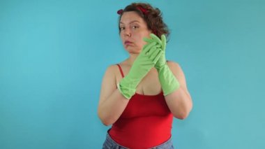 Kırmızı askılı bir kadın mavi izole bir arka planda yeşil lastik temizleme eldivenlerini çıkartıyor. Temizlik yapan kadın portresi