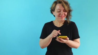 Cheerful adult woman in a black t-shirt points her finger at the mobile phone screen. Portrait of a forty year old woman on a blue isolated background.