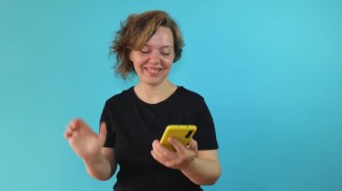 Cheerful adult woman in a black t-shirt communicates via video call via mobile phone on a blue isolated background. Woman portrait