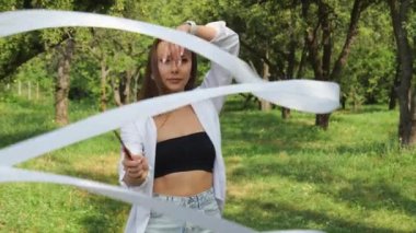 A young beautiful woman in a white shirt makes a movement with a white ribbon in nature in the garden. Slow motion portrait. Woman portrait