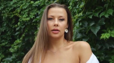 Portrait of a young beautiful woman on a background of green foliage. Woman in a white shirt outdoors in the jungle