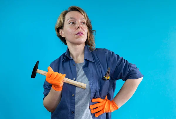 Adult woman in a shirt with a hammer on an isolated background. Woman builder in orange gloves