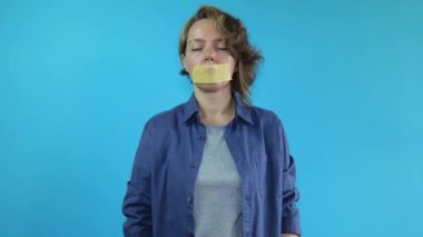 The woman's mouth is sealed with masking tape. Woman in a shirt and orange gloves on a blue isolated background. Woman portrait