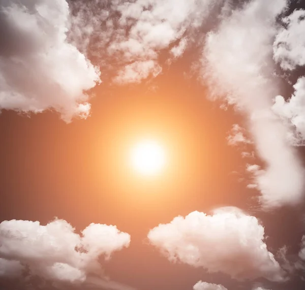 The sun shines in the center of the sky between white clouds. Sunset in the sky. Vintage style. Sky texture with big clouds. Sky background with sun