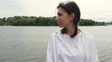 A young woman in a white shirt looks at the river. Slow motion portrait.Cheerful woman
