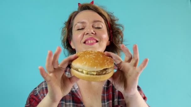 Adult Pin Woman Plaid Shirt Eats Burger Isolated Blue Background — Video