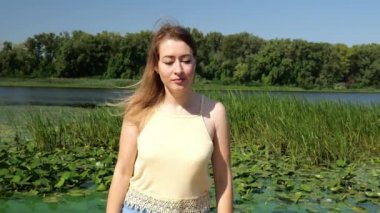 Sarı kolsuz tişörtlü genç bir kadın suyun yanında yürüyor. Doğadaki portre kadını.
