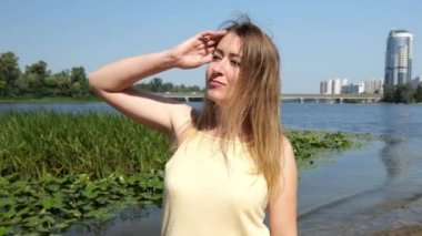 Sarı kolsuz tişörtlü genç bir kadın suyun yanında yürüyor. Doğadaki portre kadını.