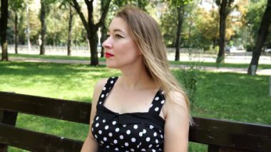 Siyah beyaz elbiseli genç bir kadın şehir parkında bir bankta oturuyor. Ağır çekimde kadın portresi