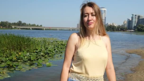 市内の川の近くに黄色のTシャツとジーンズの若い女性 スローモーションポートレート — ストック動画