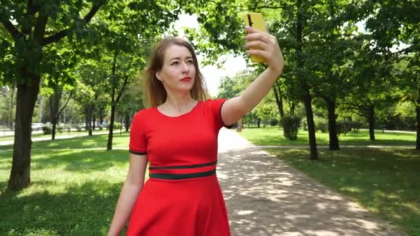 一个穿着红色衣服的年轻女子在城市公园里自拍 慢动作肖像 夏天在公园里散步的女人 — 图库视频影像