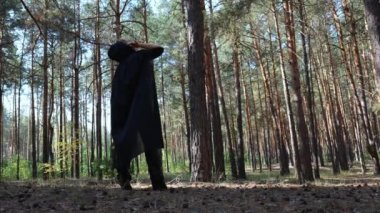 Siyah pelerinli, kukuletalı bir kadının doğadaki bir çam ormanında dikiz aynasından görünüşü. Yetişkin kadın cadılar bayramı için dans ediyor. Cadılar bayramı kadını