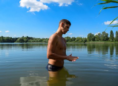 Genç bir atletik adam gölde suyun içinde duruyor. Islak, çıplak bir adam karanlık suya bakıyor. Yazın yüzen adam