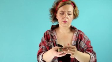 Ekose gömlekli kadın izole edilmiş mavi arka planda dolar sayıyor. Yetişkin bir kadının portresi. Kağıt dolar atar