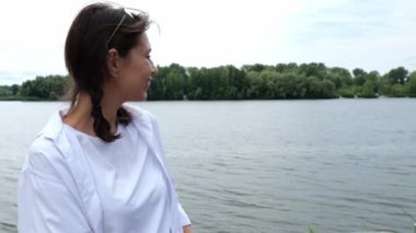 Suyun yanında beyaz gömlekli esmer bir kadının portresi. Yavaş çekim portresi. Suya bakan kadın.