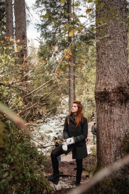 Kışın siyah bir sırt çantasıyla dağlarda çam ağaçlarıyla çevrili bir kız.