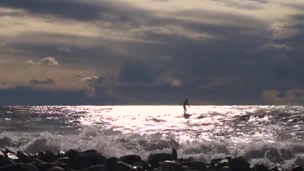 Ein Surfer in der Abendsonne versucht mit einem Paddel auf einer Welle zu reiten — Stockvideo