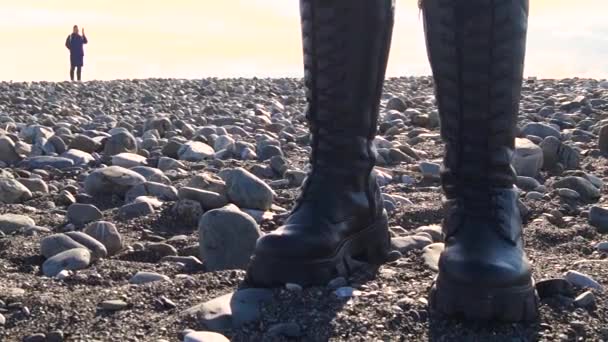 Крупный план, ноги девушки в черных сапогах, стоящей на скалистом пляже. — стоковое видео