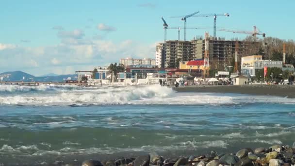 Obrovská vlna narazí na skalnatou pláž na pozadí města ve výstavbě — Stock video