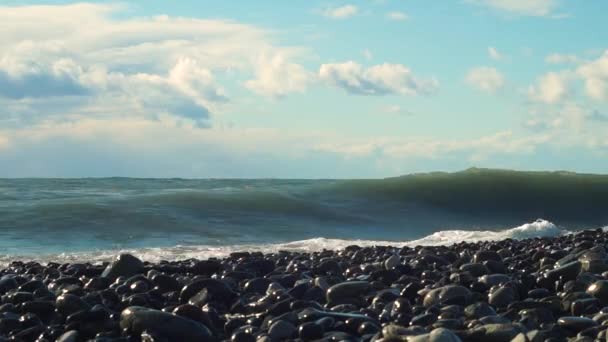 大きな海の波がビーチの岩にぶつかり、青い空が破片で溢れています。 — ストック動画