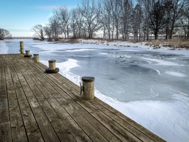 Rıhtımdan deniz fenerine giden küçük bir köprü ile küçük bir ada görülebilir. Donmuş nehir, suyun yüzeyini kaplayan karla kaplı..