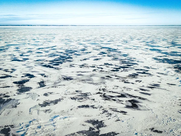 雪は湖の表面の周りに明るい青い澄んだ空の下で裸の氷のパッチで吹いている — ストック写真