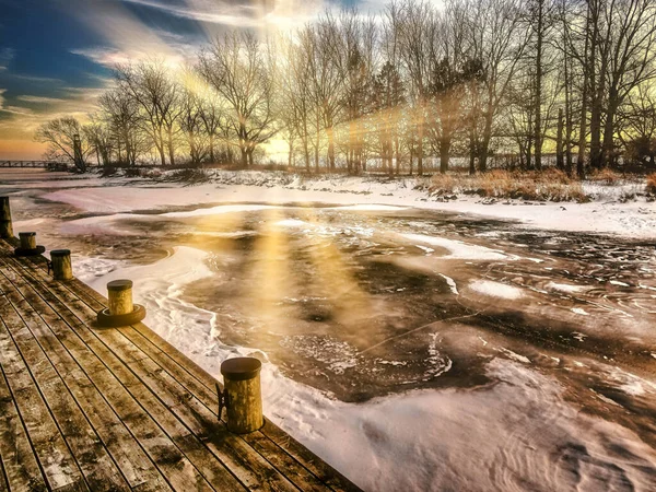 Karla kaplı buzla kaplı donmuş yüzey. Güneş ağaçları ve donmuş arazinin buzlu yüzeyini aydınlatıyor. Adanın köşesinde terk edilmiş küçük bir deniz feneri görülebilir..