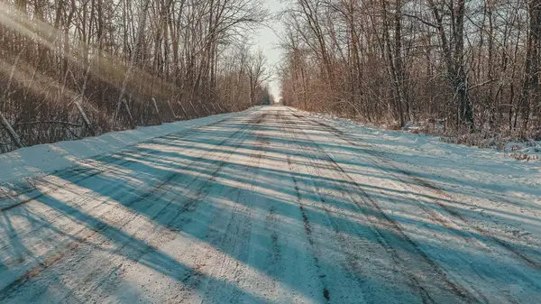 雪に覆われた1車線の未舗装の道路を運転太陽が木を通して輝くように雪で覆われた — ストック写真