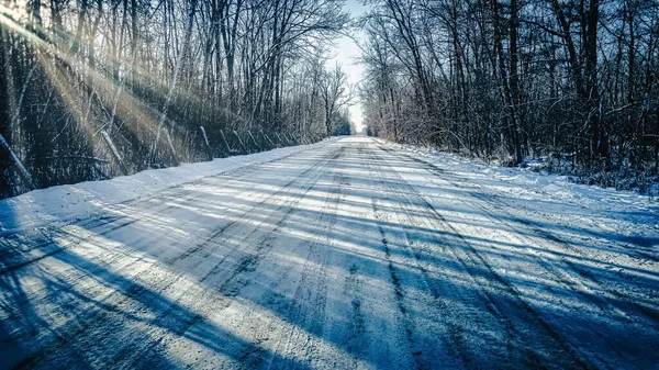 雪に覆われた未舗装の道路で 太陽が木を通して輝いている — ストック写真