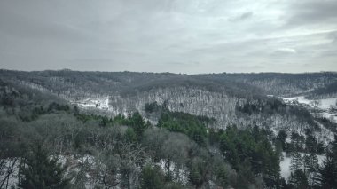 Karla kaplı tepelerin üzerindeki bulutlu gökyüzünde sadece kışın yeşil renkler sergilenir.