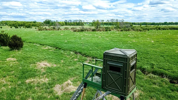 Spring view with a cloudy blue sky above a empty green grassy field. A hunting blind stands over looking all of it