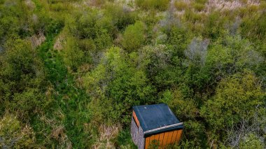 Doğal bir çayırda bulundu. Terk edilmiş bir av kulübesi, yanında eski çimenlik bir patikayla çürüyor..