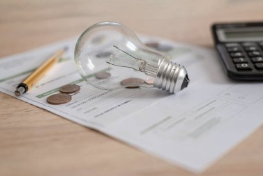 Ampullü elektrik faturası, birkaç bozuk para, hesap makinesi ve kalem masanın üzerinde. Elektrik fiyatları ve vergi ödemeleri kavramı.