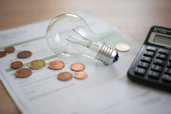 Electricity bill with light bulb, several coins and calculator on the desk. Concept of electricity prices and tax payments.