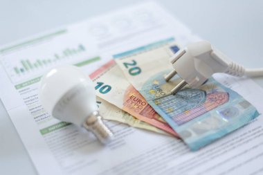 Bir elektrik faturasında beyaz bir başlık, bir ampul ve euro banknotları. İkametgah müşterileri ve iş kullanıcıları için elektrik maliyetinde artış. Elektrik faturaları. Elektrik fiyatları kavramını artırıyor.