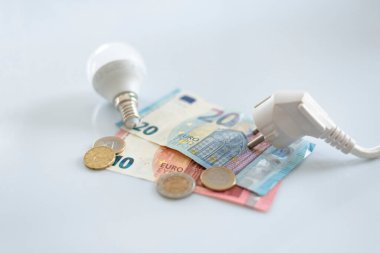 Avro banknotlarına beyaz elektrik kapağı ve ampullü çeşitli madeni paralar. İkametgah müşterileri ve iş kullanıcıları için elektrik maliyetlerinde artış. Elektrik faturaları. Elektrik fiyatları kavramını artırıyor.