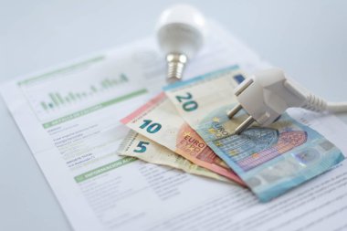Bir elektrik faturasında beyaz bir başlık, bir ampul ve euro banknotları. İkametgah müşterileri ve iş kullanıcıları için elektrik maliyetinde artış. Elektrik faturaları. Elektrik fiyatları kavramını artırıyor.