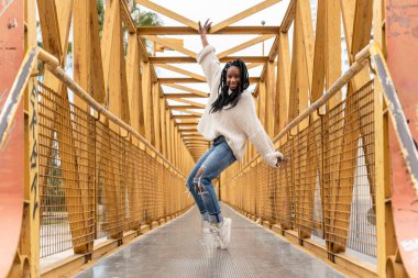 Sarı bir köprüde dans eden gülümseyen Afro-Amerikalı bir kadın.