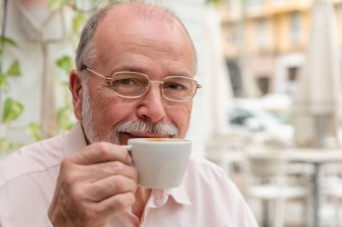 Gülümseyen yaşlı bir adamın portresi. Gözlüklerle emekli olmuş. Kahve içiyor ve kameraya bakıyor.