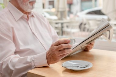 Kahve dükkanında kahvesini içerken günlük gazete okuyan tanınmayan yaşlı bir adam.