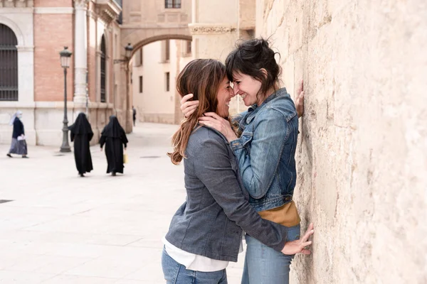 Valencia sokaklarında gülüp kucaklaşan genç lezbiyen çift, arka planda rahibeler, gay konsepti.