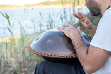 Geleneksel çelik bir pervane çalan, gölün kıyısında oturan tanınmayan bir adamın yakından ve yandan görünüşü, rahatlatıcı bir müzik.