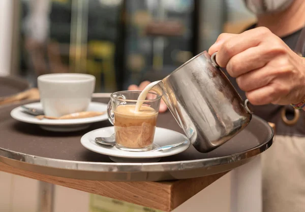 waiter preparing coffee by pouring milk into a coffee cup