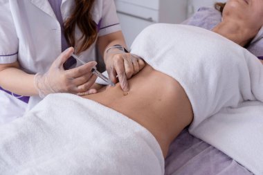 Kadın karnına vücut mezoterapisi enjeksiyonları, selülit tedavisi. Güzellik salonunda kadın estetiği..